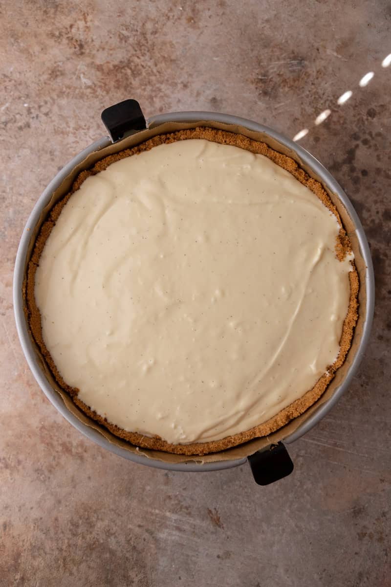 Cheesecake filling poured and smoothed over the graham cracker crust in a springform pan.
