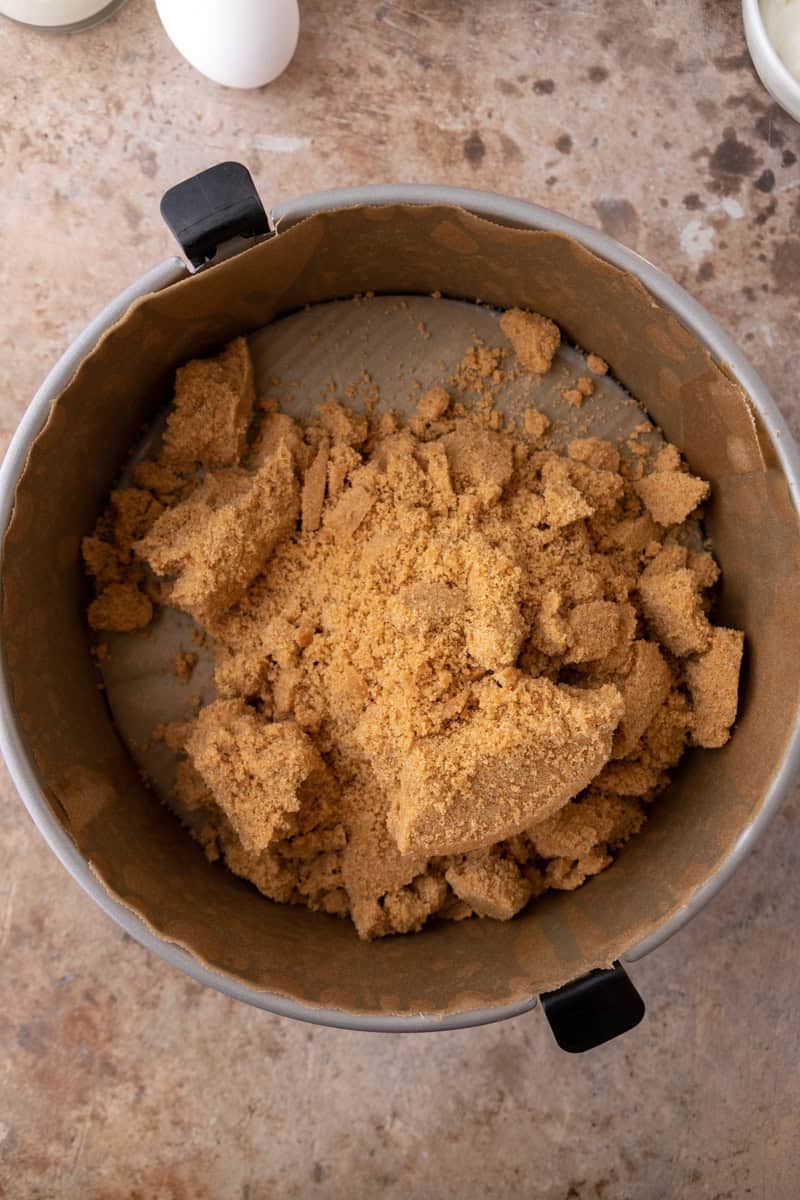 Buttery graham cracker crumbs in a parchment-lined springform pan, ready to press into a crust.