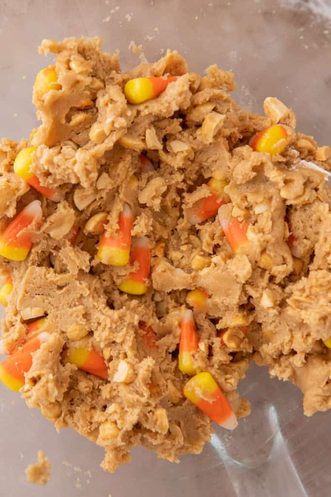 Candy corn cookie dough in a glass bowl with peanuts and candy corn folded evenly throughout.