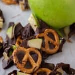 Pieces of caramel apple bark scattered on a baking sheet with parchment paper next to a Granny Smith apple.