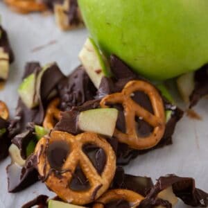 Pieces of caramel apple bark scattered on a baking sheet with parchment paper next to a Granny Smith apple.