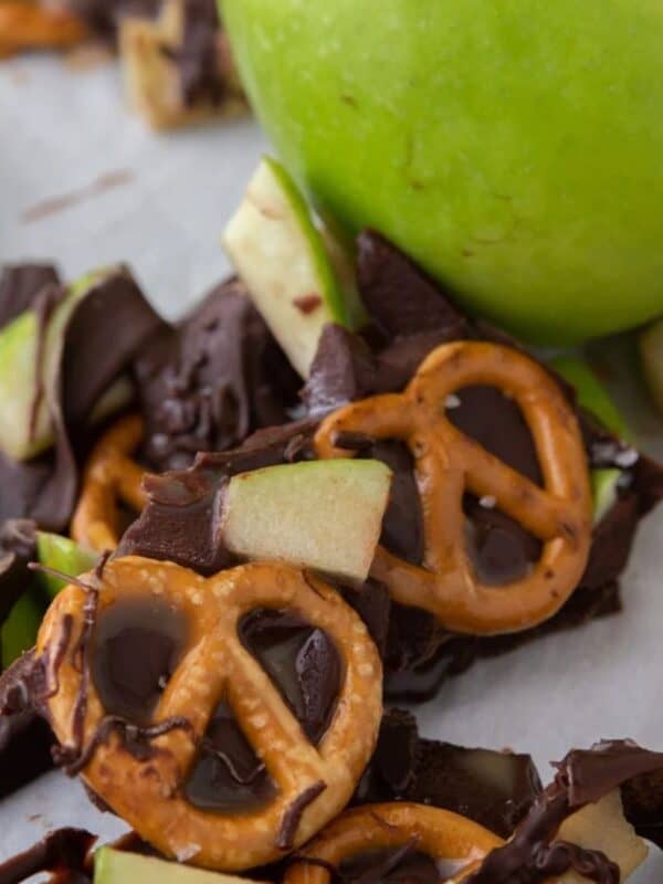 Pieces of caramel apple bark scattered on a baking sheet with parchment paper next to a Granny Smith apple.