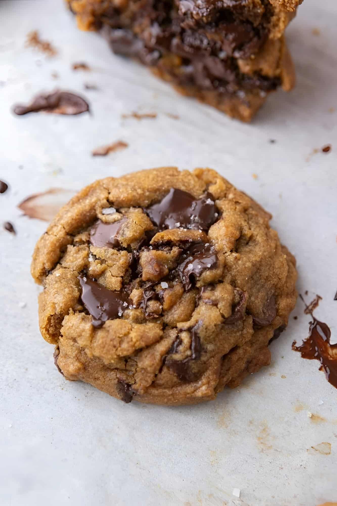 Chewy brown butter pumpkin chocolate chip cookies cooling on parchment with melted chocolate pooling on top.