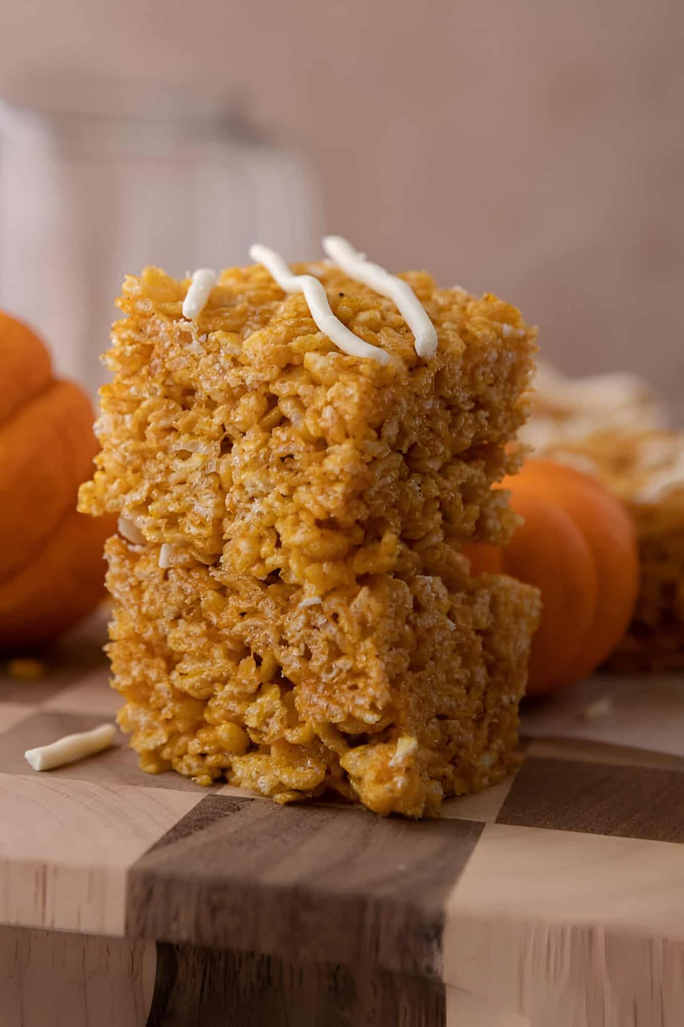 Pumpkin rice krispie treats cut into squares stacked with white chocolate drizzled across the tops.