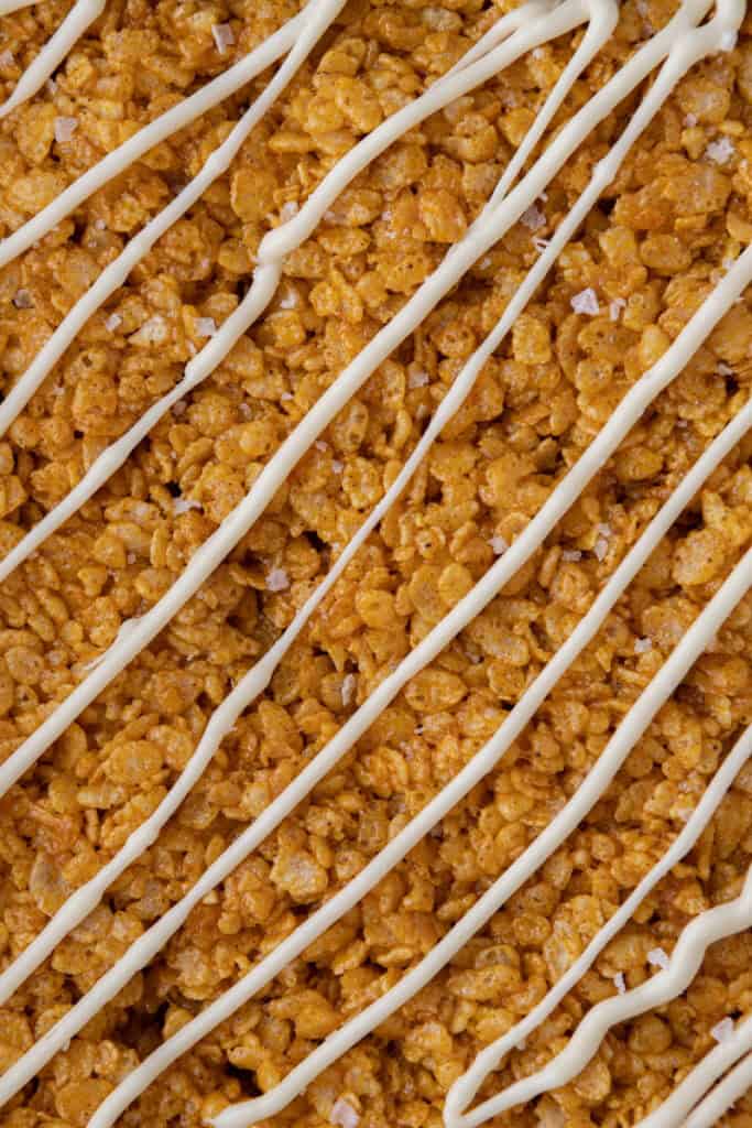 Melted white chocolate drizzled in thin lines over the pressed pumpkin cereal mixture.