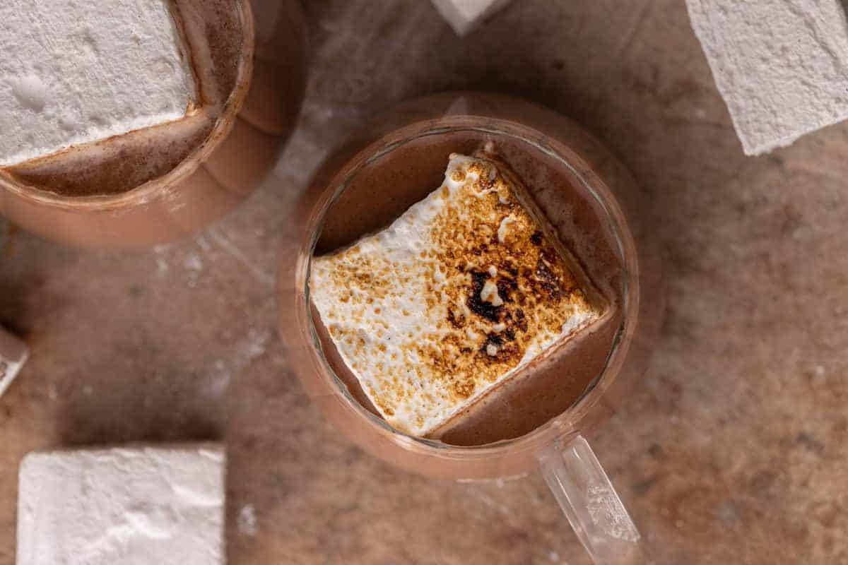 Overhead view of hot cocoa in a glass mug topped with a toasted marshmallow.
