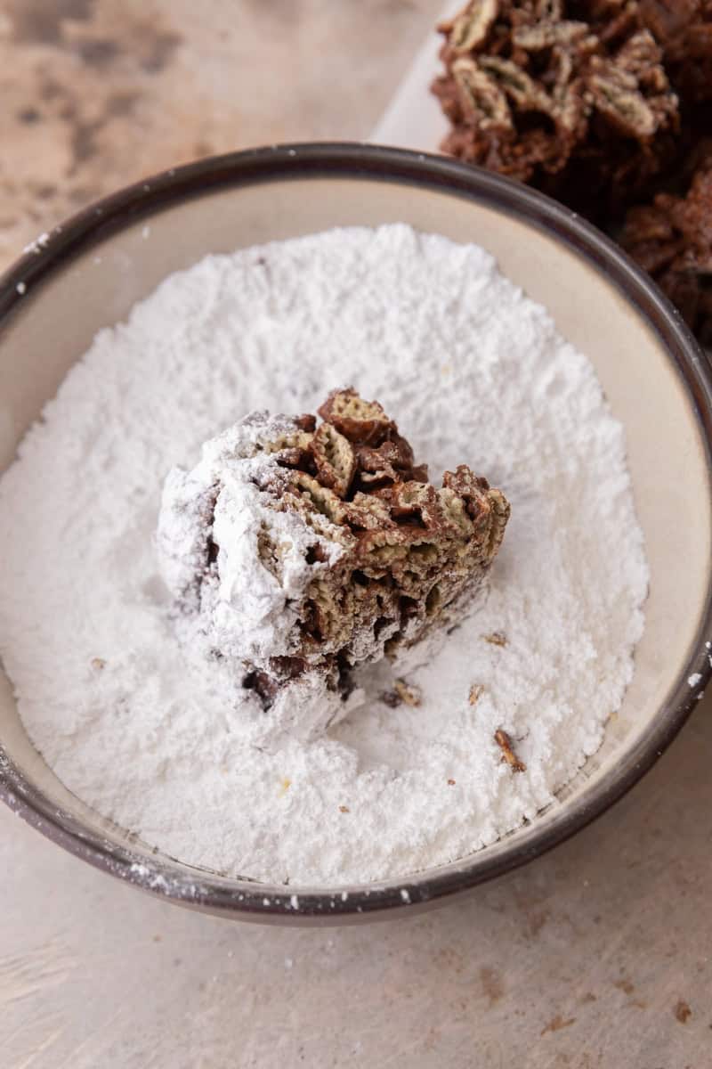A muddy buddy bar being tossed in a bowl of powdered sugar.