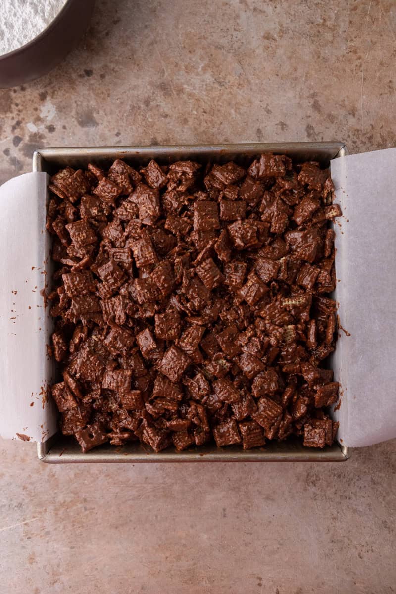 Chocolate-coated cereal pressed into an even layer in a parchment-lined square pan.