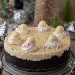 A full peppermint cheesecake topped with truffles and whipped cream, set among holiday decorations.