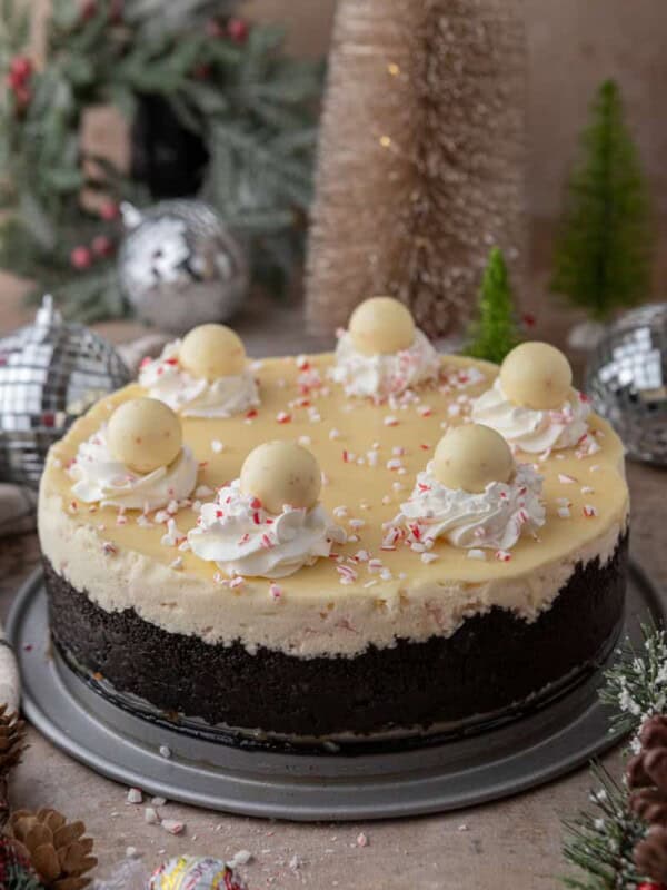 A full peppermint cheesecake topped with truffles and whipped cream, set among holiday decorations.