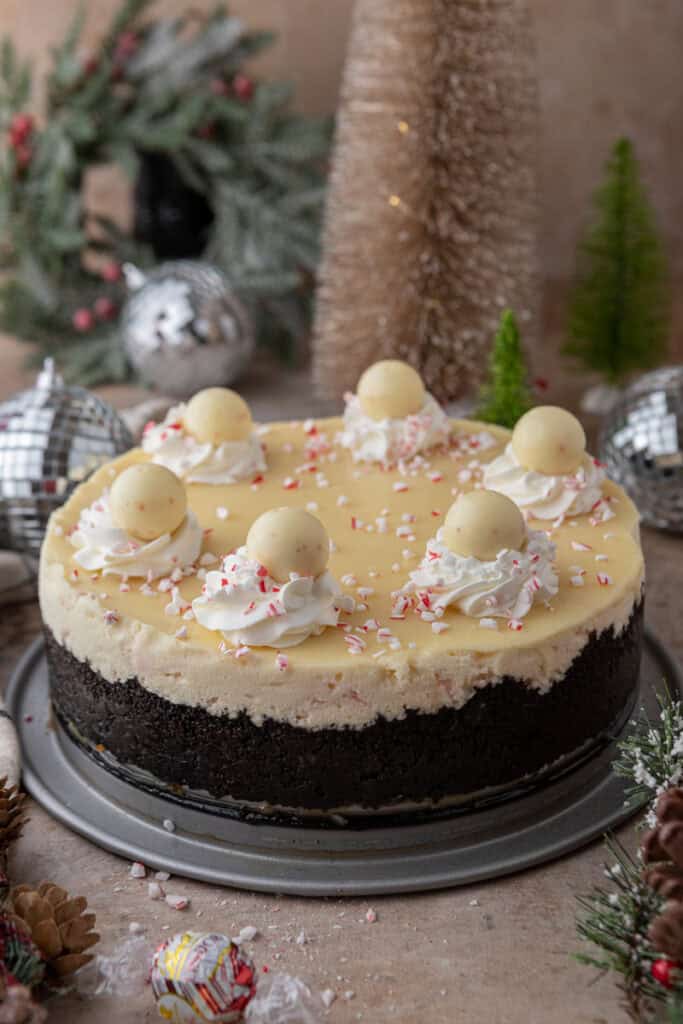 A full peppermint cheesecake decorated with whipped cream swirls, crushed candy canes, and Lindt peppermint truffles.