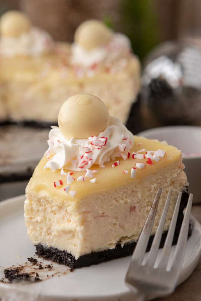 A close-up slice of peppermint cheesecake with Oreo crust topped with whipped cream, crushed candy canes, and a white chocolate truffle.