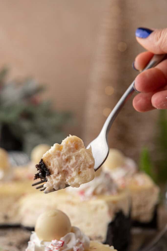 Fork holding a bite of peppermint cheesecake with Oreo crust in front of the whole cheesecake.