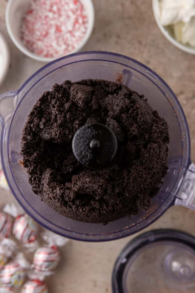 Crushed Oreo cookies inside a food processor ready to be mixed with butter for the cheesecake crust.