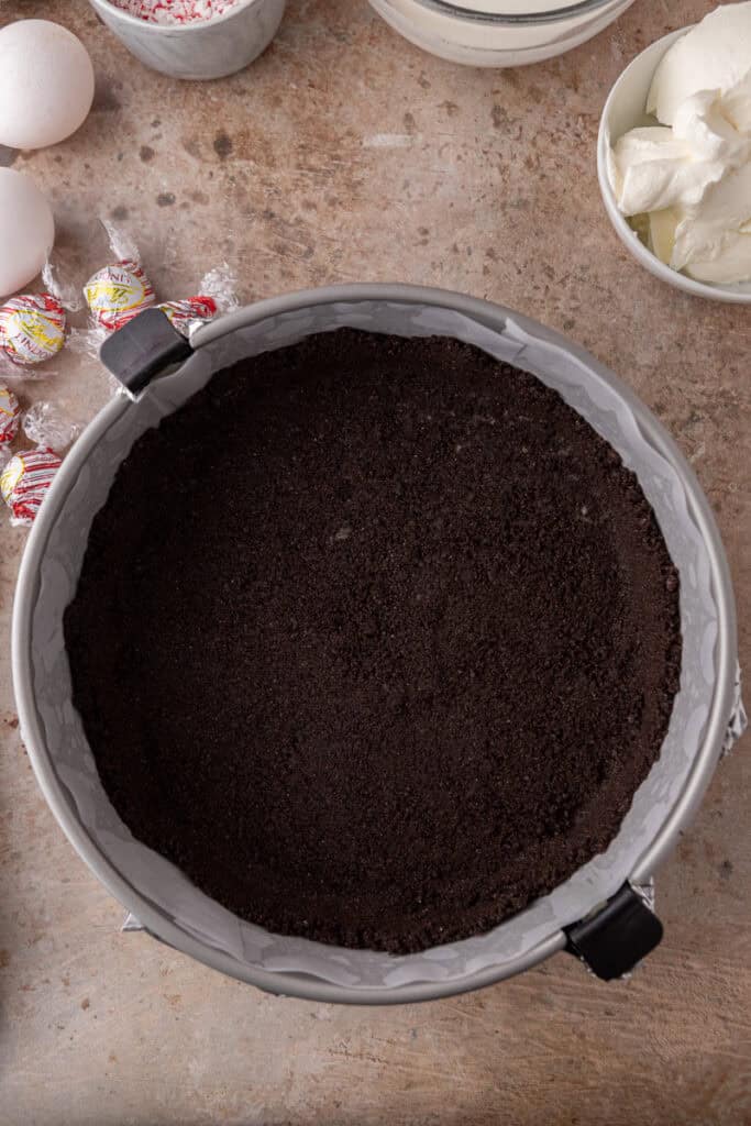 Pressed Oreo cookie crust lining the bottom of a springform pan, ready to be baked.