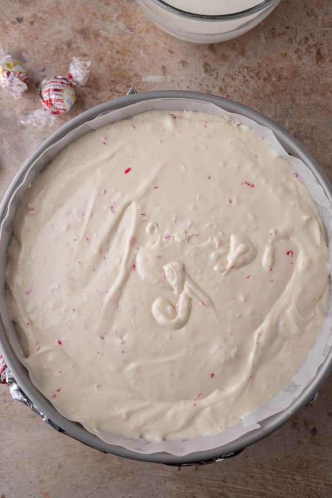 Unbaked peppermint cheesecake batter spread evenly in a parchment-lined springform pan.