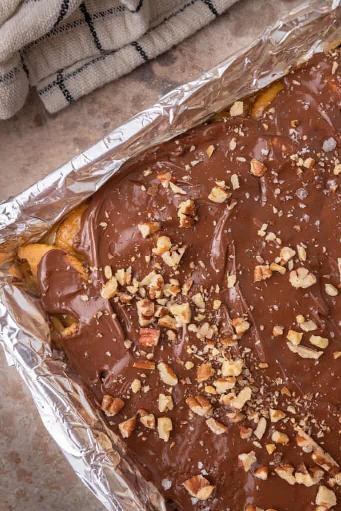 Pan of homemade Christmas crack topped with melted chocolate and chopped pecans.