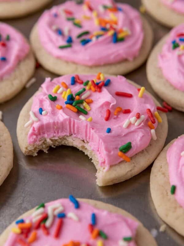 Soft sour cream sugar cookie with pink frosting and rainbow sprinkles, with a bite taken out to show the tender interior.