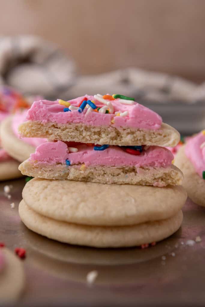Soft sour cream sugar cookies stacked with a frosted cookie cut open to show the fluffy interior.
