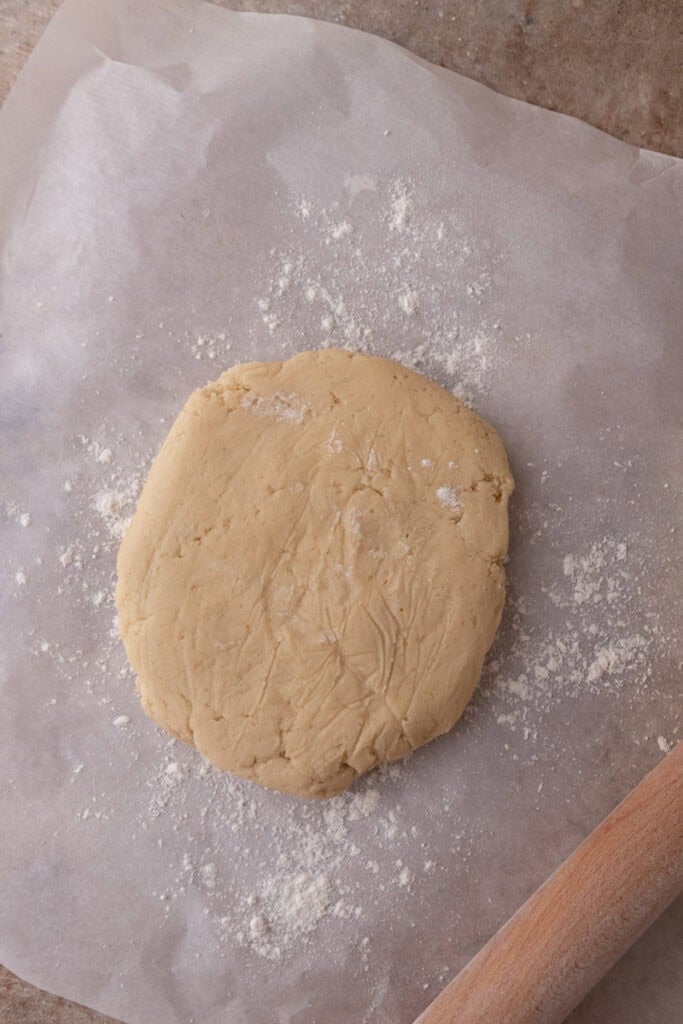 Sugar cookie dough shaped into a thick disc on parchment paper before chilling.
