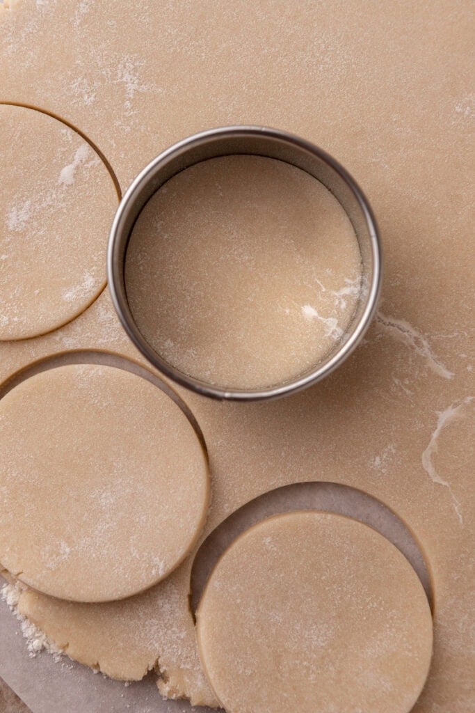 Rolled-out sour cream sugar cookie dough with round cookie cutter pressing out circles.
