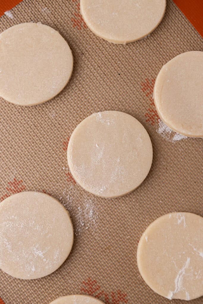 Round sour cream sugar cookie dough cutouts arranged on a baking sheet before baking.
