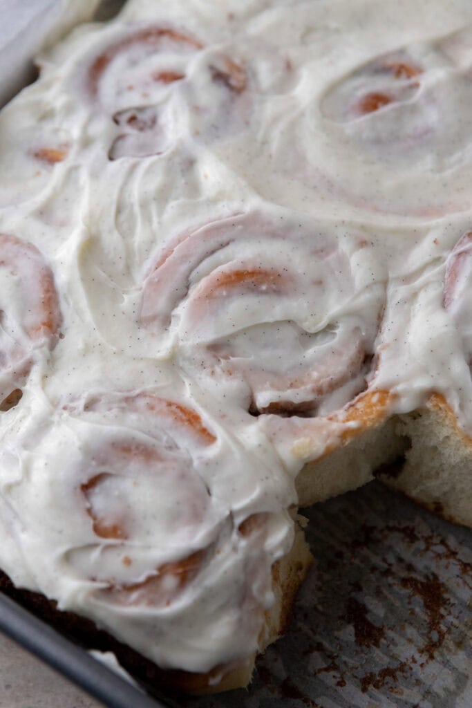 Pan of frosted sourdough discard cinnamon rolls with one roll removed showing soft layers