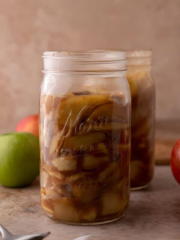 Glass jar filled with homemade apple filling, diced apples coated in thick cinnamon brown sugar syrup.