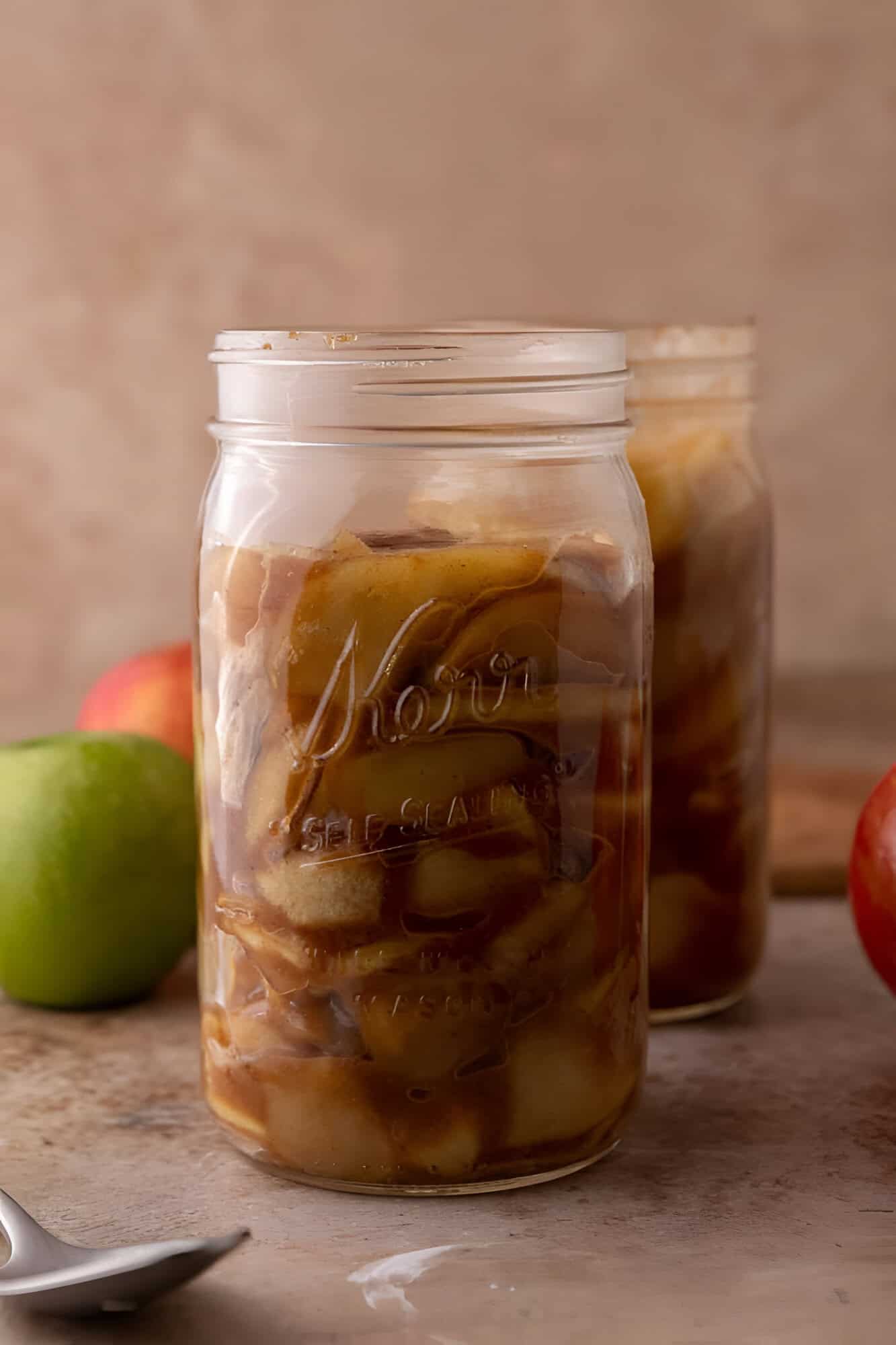 Glass jar filled with homemade apple filling, diced apples coated in thick cinnamon brown sugar syrup.