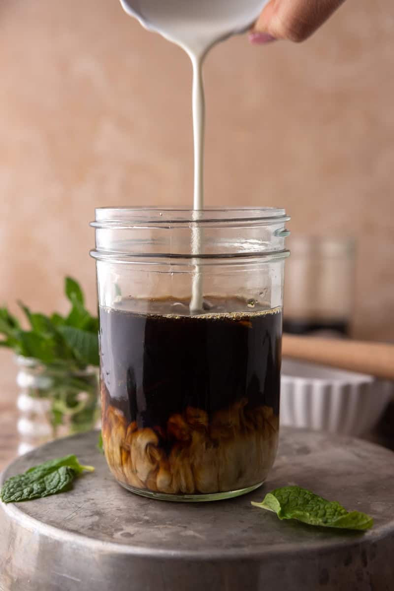 Heavy cream poured into a jar of cold brew, swirling into the dark coffee.