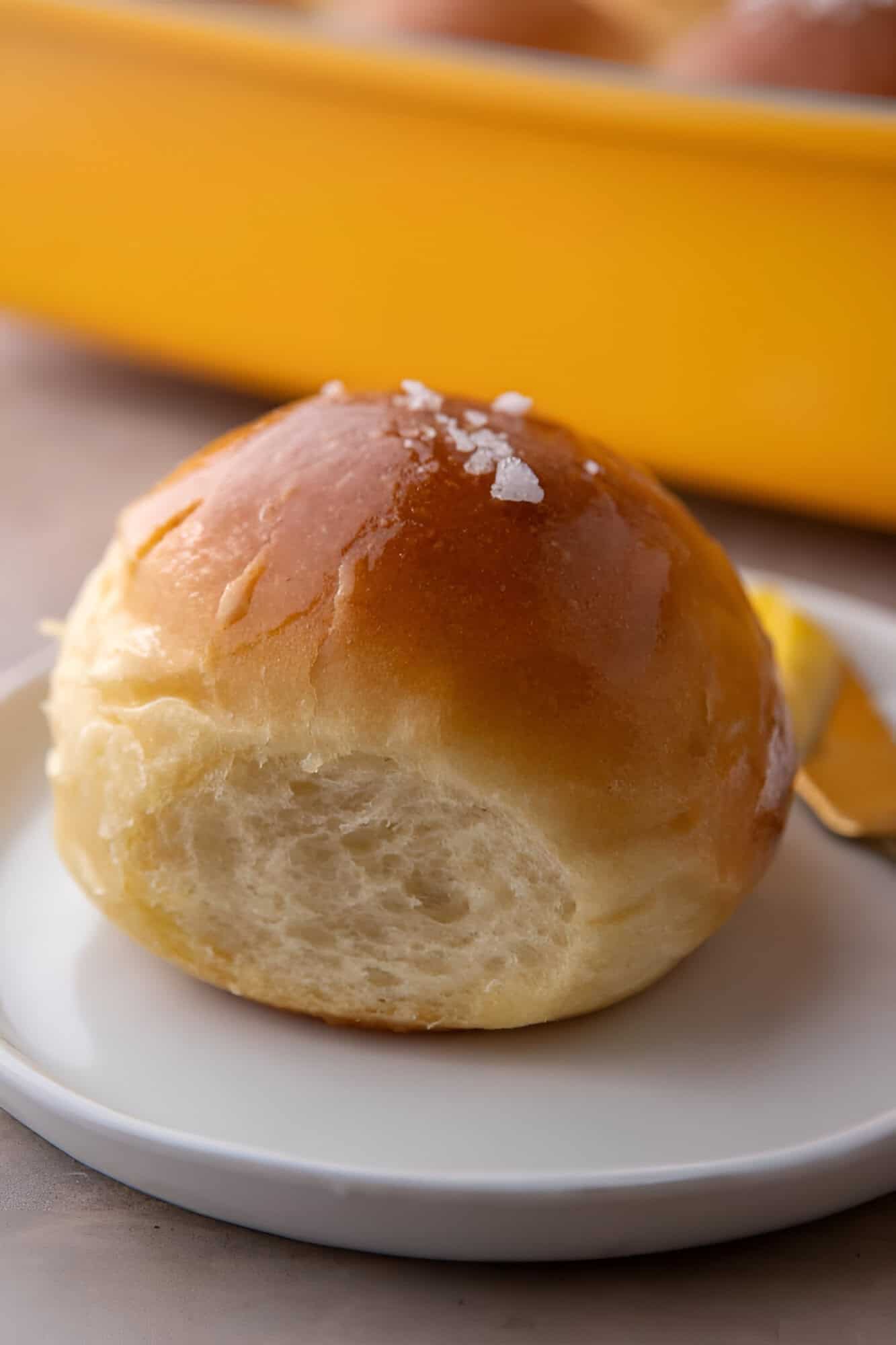 Golden soft dinner rolls brushed with butter and topped with flaky salt in a white serving plate.