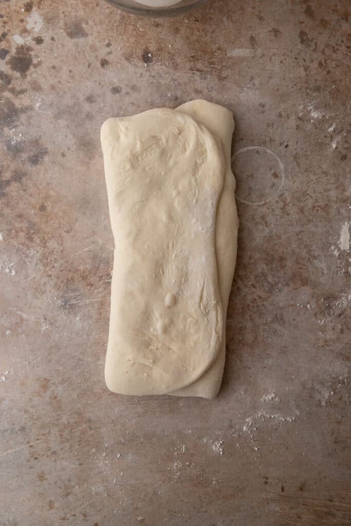 stretched out dough folded on a floured surface