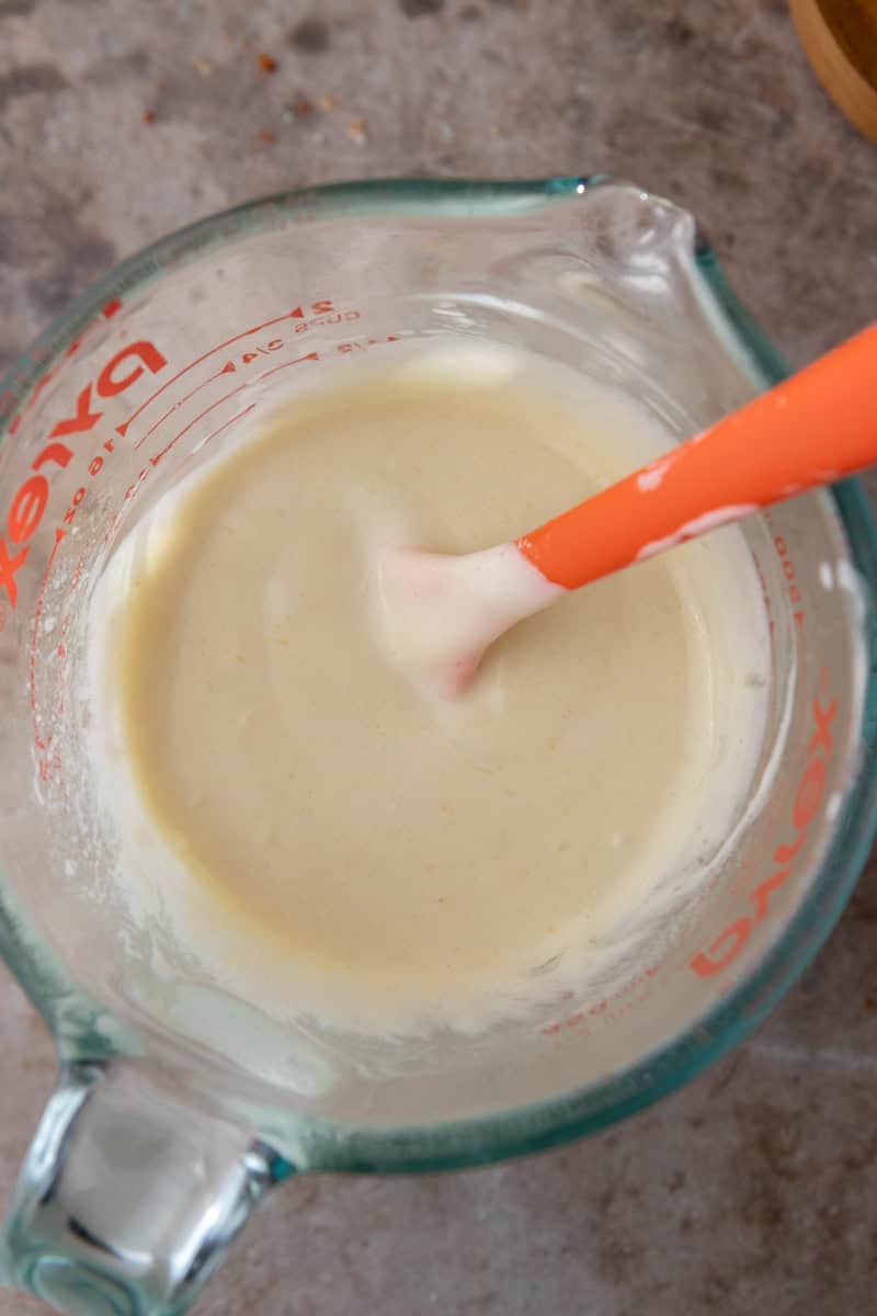 Smooth sourdough discard and butter mixture stirred with an orange spatula in a glass measuring cup.