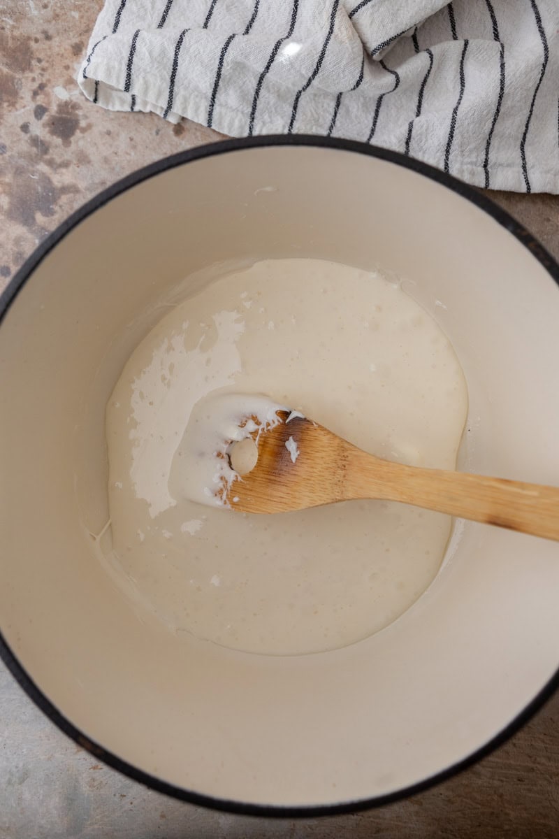 Melted marshmallows stirred smooth in a white pot with a wooden spoon.