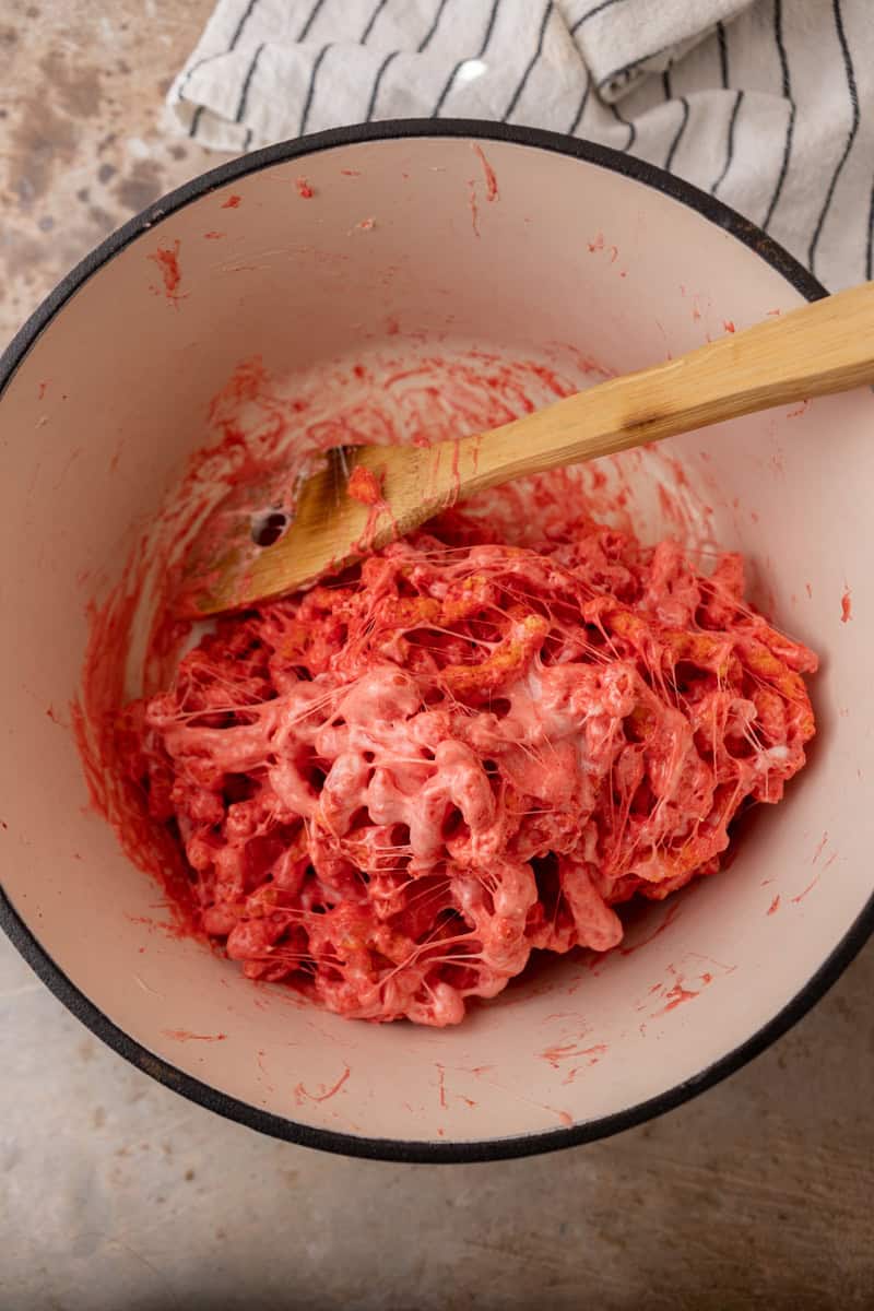Flamin' Hot Cheetos stirred into gooey melted marshmallow in a white pot.