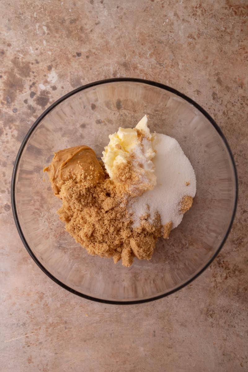 Peanut butter, brown sugar, butter, and granulated sugar in a glass mixing bowl before creaming.