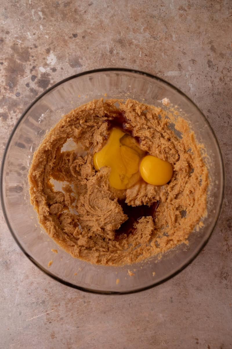 Egg and vanilla added to the creamed peanut butter and sugar mixture in a glass bowl.