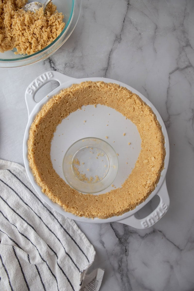 Golden Oreo crumbs pressed up the sides of a white Staub pie dish with a small glass in the center.