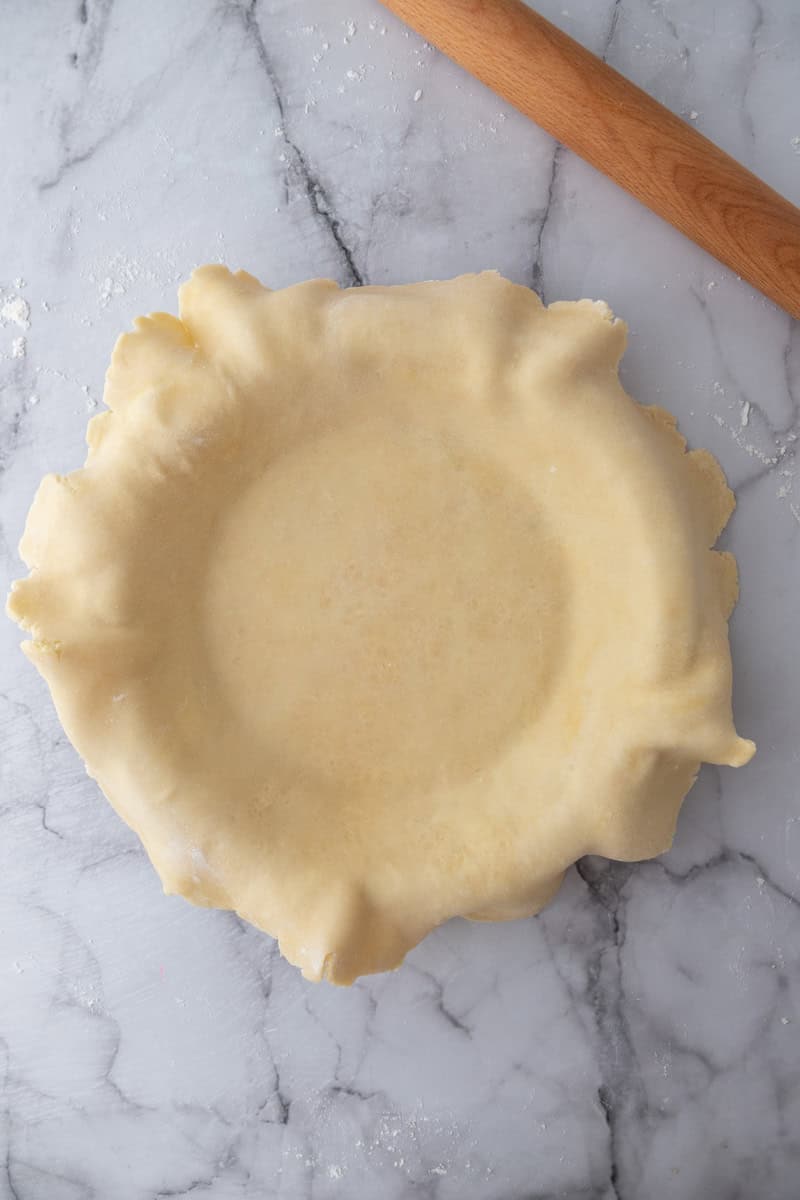 Rolled pie dough draped into a pie plate with the edges hanging over the sides.