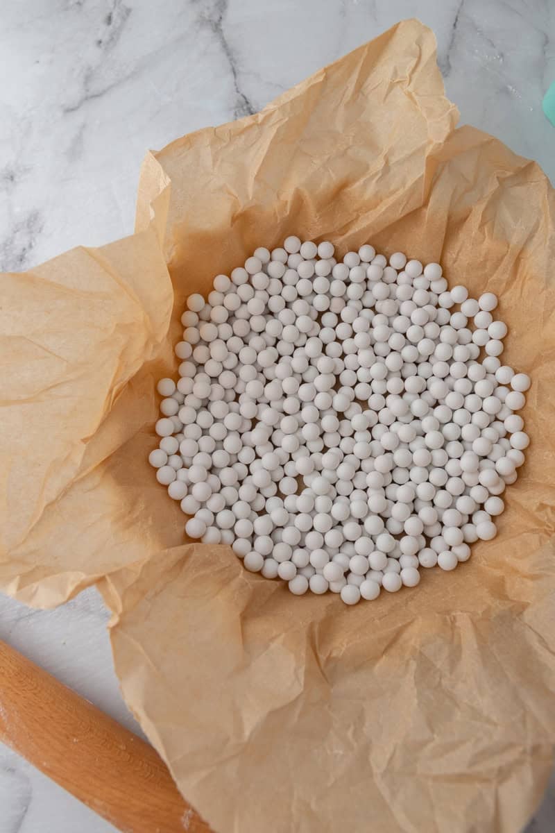 Pie crust lined with parchment paper and filled with ceramic pie weights.
