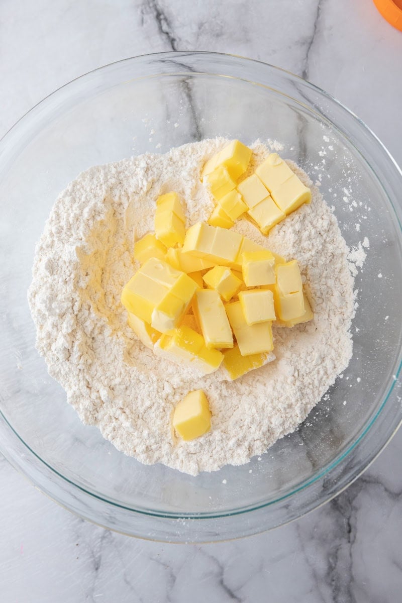 Cubes of cold butter added to the flour mixture in a glass bowl.