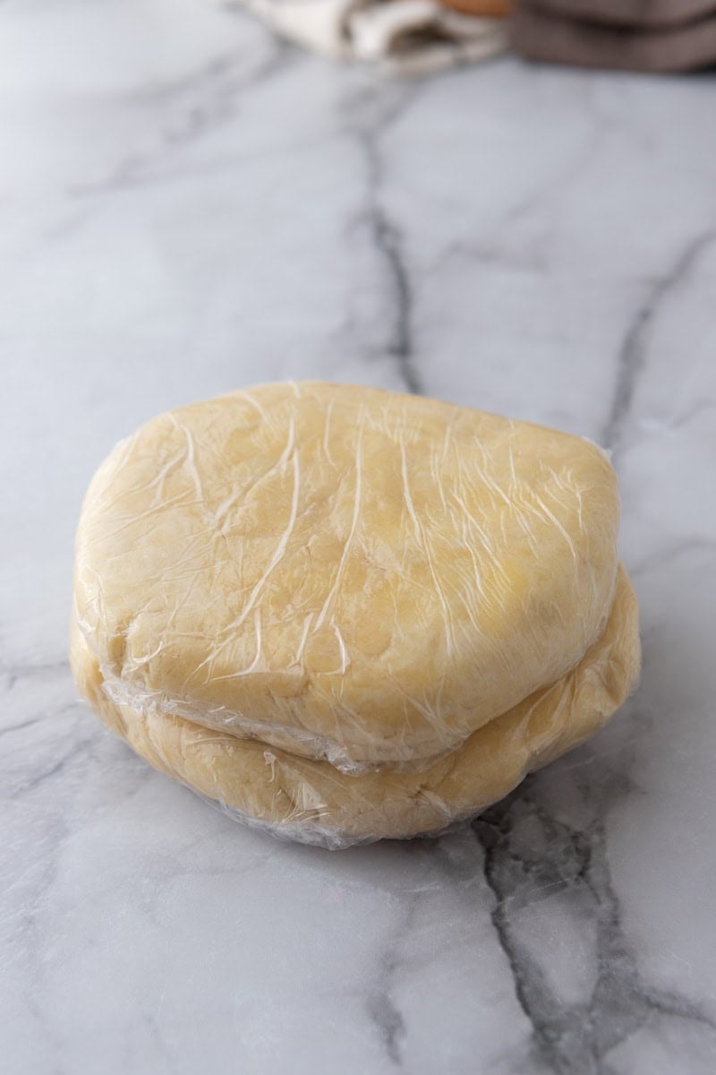 Two discs of sourdough pie dough stacked and wrapped in plastic wrap.
