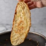 A slice of sourdough croissant bread being toasted on a stove-top pan as you see the buttery layers on the inside.