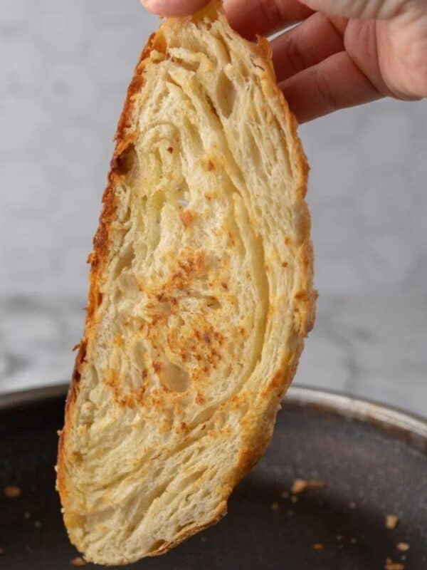 A slice of sourdough croissant bread being toasted on a stove-top pan as you see the buttery layers on the inside.