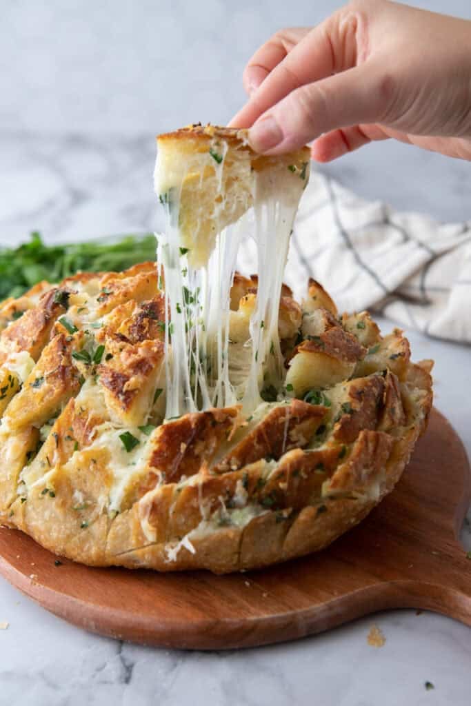 Hand pulling apart baked sourdough garlic bread with melted mozzarella stretching