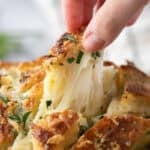 Hand pulling apart a piece of cheesy sourdough garlic bread with melted mozzarella stretching