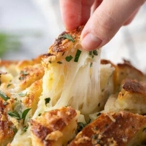 Hand pulling apart a piece of cheesy sourdough garlic bread with melted mozzarella stretching