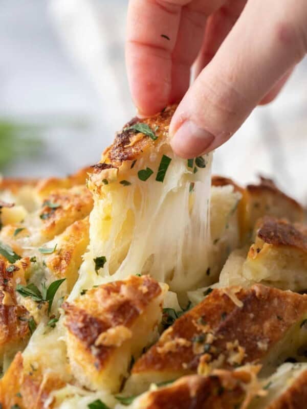 Hand pulling apart a piece of cheesy sourdough garlic bread with melted mozzarella stretching