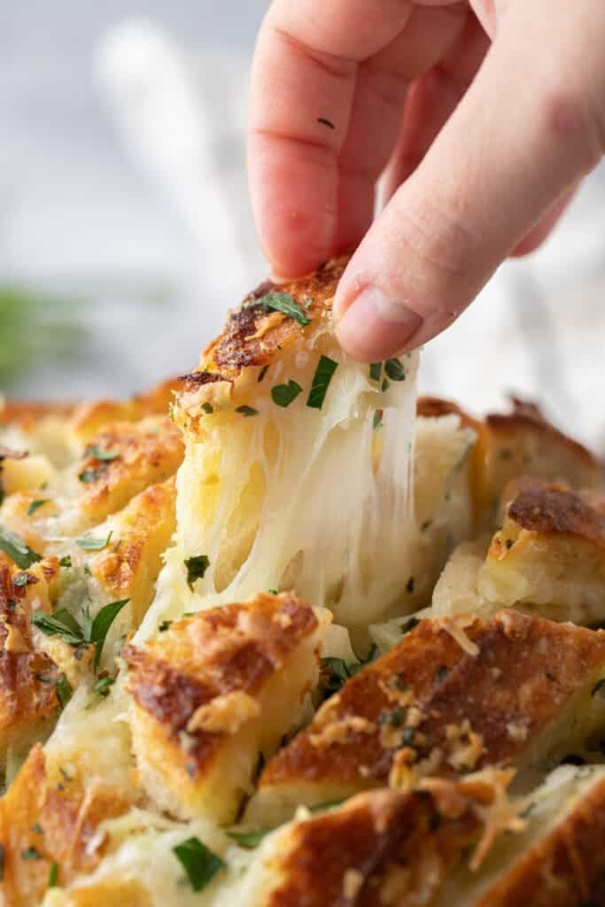 Hand pulling apart a piece of cheesy sourdough garlic bread with melted mozzarella stretching