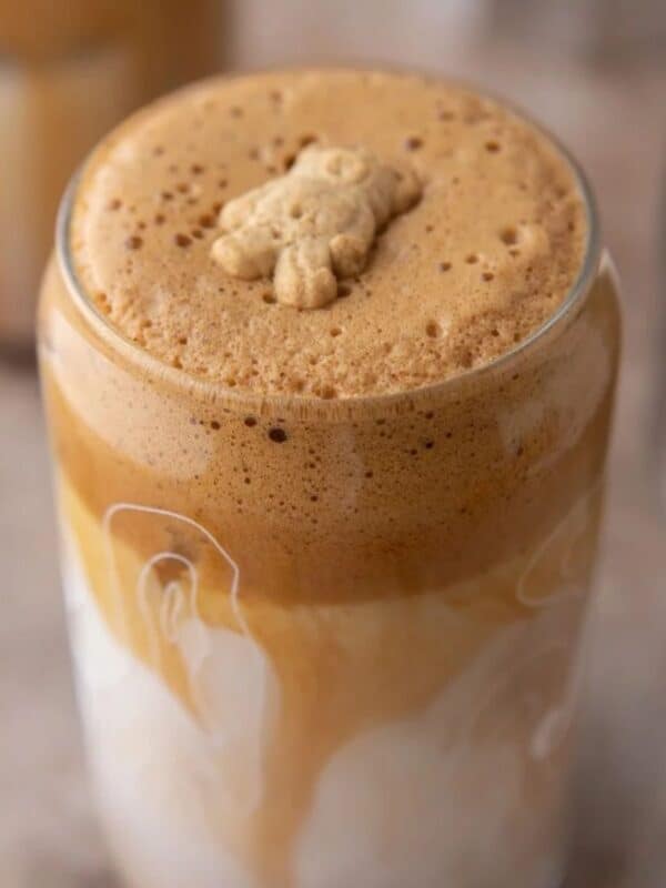 A tall glass of Teddy Graham Latte showing distinct layers and foamed top with a garnish of a single Teddy Graham cracker.